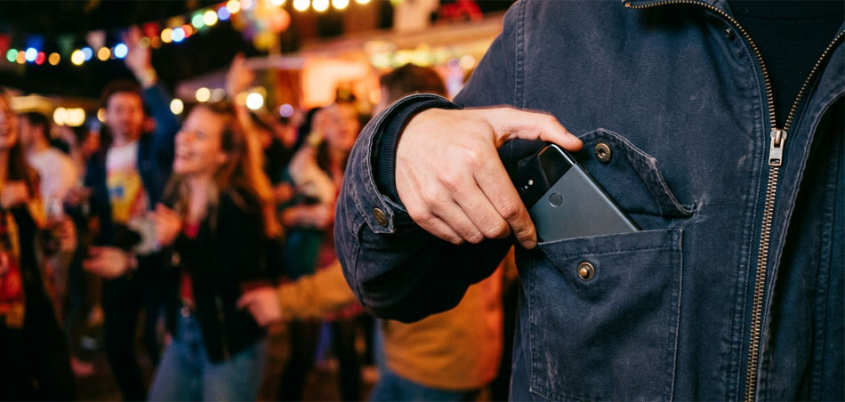 Feiernde Menschen im Hintergrund, im Vordergrund gleitet ein Handy in die Jackentasche